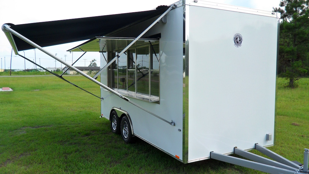 A white trailer with awning open on grass.