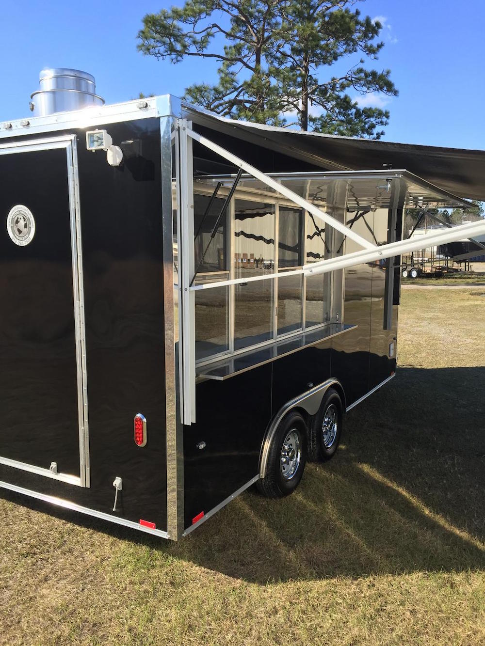 A black trailer with awning and lights on the side.