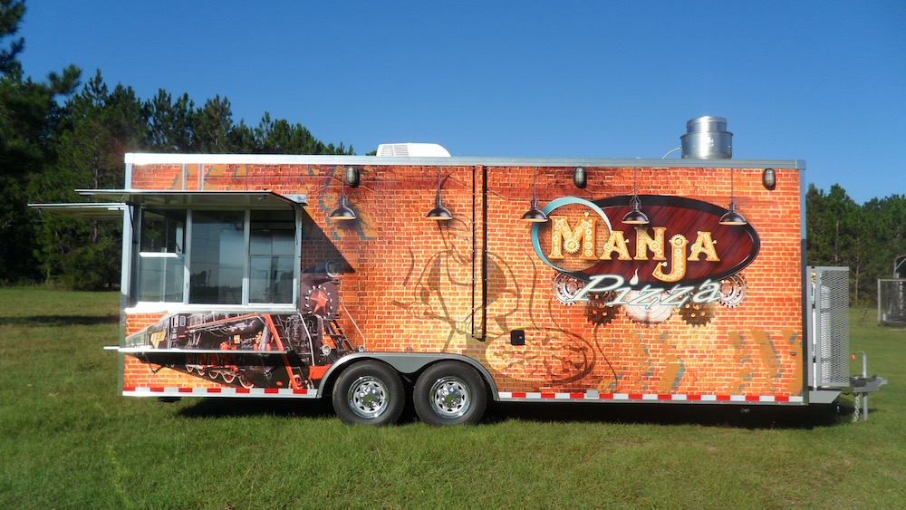 A food truck parked in the grass near trees.