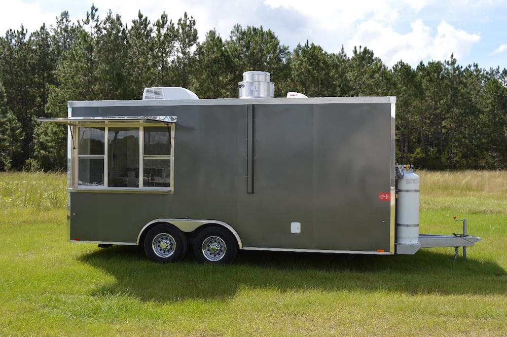 A gray trailer parked in the grass near trees.